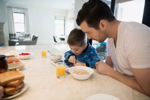 father and son using tablet while eating breakfast
